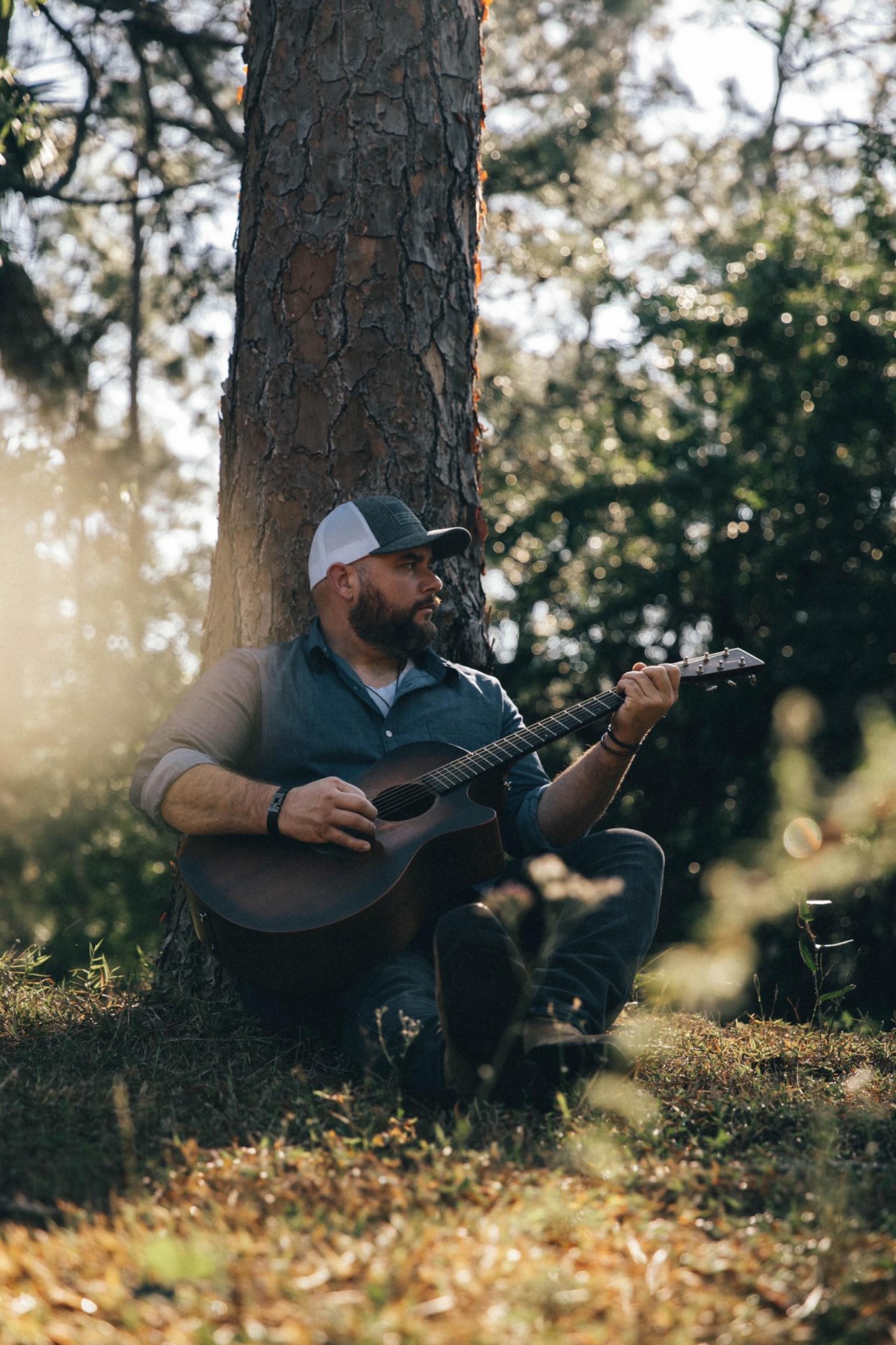 NateMichaels2022 Nate Michaels playing guitar sitting against a tree.