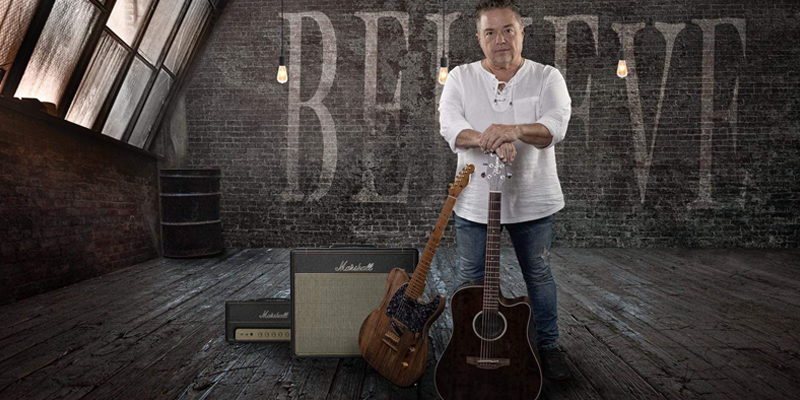 Brian Hughes with a guitar and amp inside a an older brick buidling.