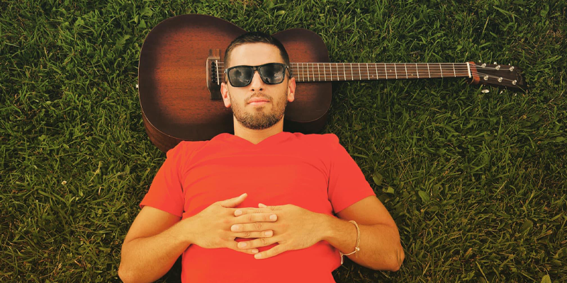 KevinLudwig Kevin Ludwig wearing sunglasses laying in the grass with the guitar behind his head as a headrest.